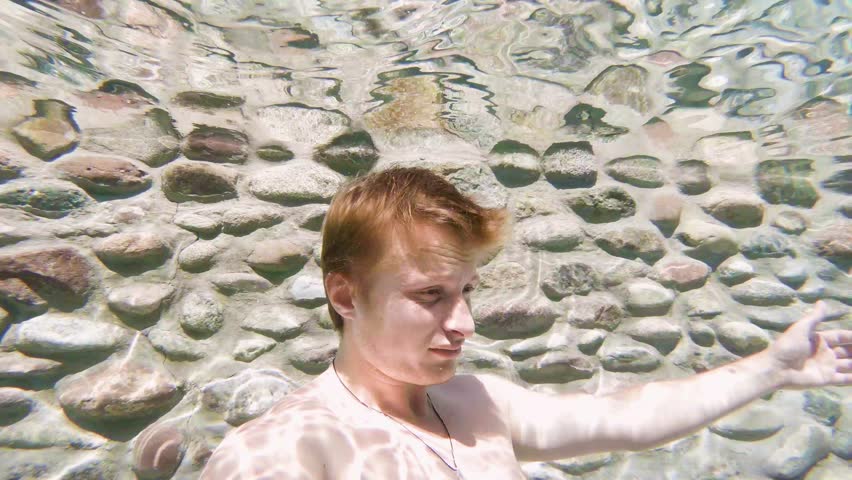 young man with red hair underwater shows thumb and smiles