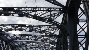 Steel arched bridge with girders and supports, bottom view against cloudy sky