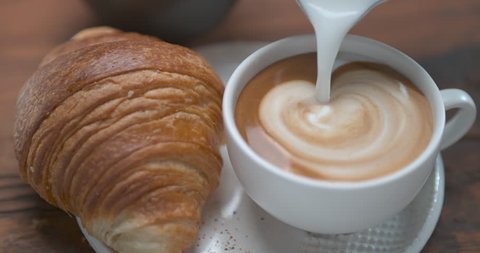 Mouth watering latte being poured in cup next to butter croissant ultra slow motion closeup with 4k Phantom Flex camera