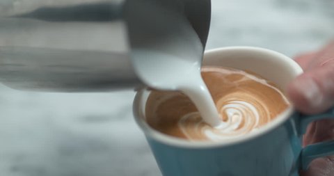 Barista making latte milk design by pourring milk in blue cup in ultra slow motion closeup with 4k Phantom Flex camera