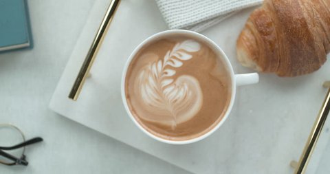 Pretty latte leaf design in white cup next to butter croissant and reading glasses ultra slow motion closeup with 4k Phantom Flex camera.