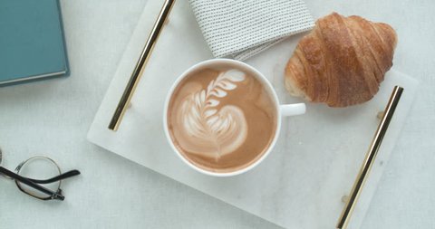 Pretty latte leaf design in white cup next to butter croissant and reading glasses ultra slow motion closeup with 4k Phantom Flex camera