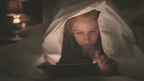 Teenage girl in bed playing a tablet in social internet in the dark light. Close up of little girl watching video on the digital tablet at night.