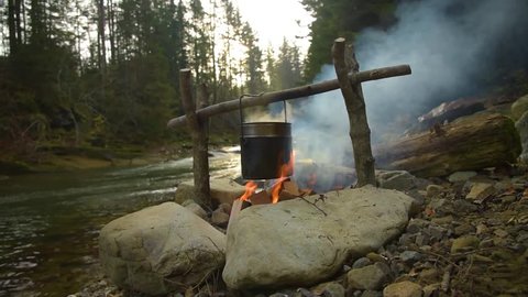 Cooking on bonfire. Campfire near mountain river. Camping Fire On The River Bank
Fire And Campsite By River In The Forest. Concept adventure in the wild nature. Vacation concept