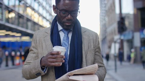 Mature business man reading a newspaper and drinking as he walks in the city
