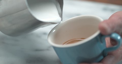 Barista making latte by pourring milk in blue cup in ultra slow motion closeup with 4k Phantom Flex camera