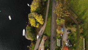 Panoramic bird's-eye aerial view of traffic road between a field and some trees, with a marina