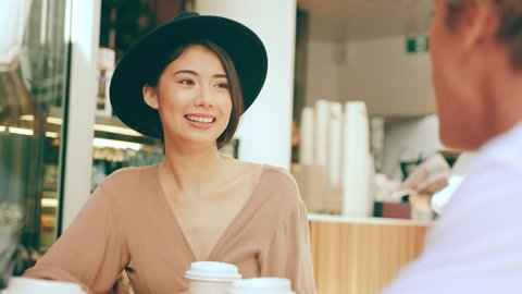 Stylish smiling woman drinking coffee with her friends in sitting area near cafe. Close up shot on 4k RED camera.