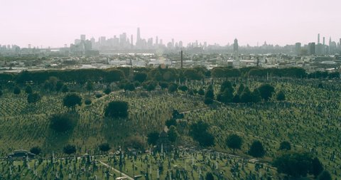 Aerial view of green cemetery with Manhattan skyline in distance in New York during the day under blue skies. Wide shot on 4K RED camera.