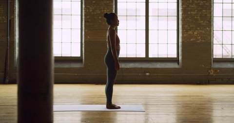 Asian yoga woman doing sun salutation in beautiful wood industrial space during the day. Wide to long shot on 4K RED camera.