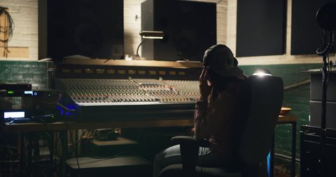 Young Asian woman sound editor works late into the night in mixing studio over professional mixing boards. Medium to long shot on 4K RED camera.