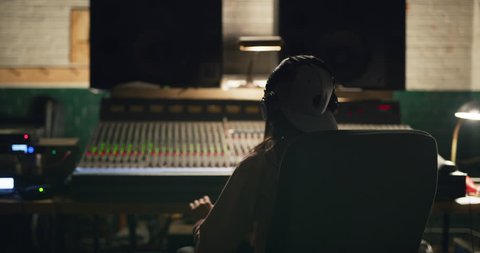 Music producer swaying to music she is working on at night in recording studio over professional mixing board. Medium shot on 4K RED camera.
