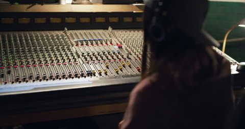 Sound engineer listening and grooving to music in recording studio using professional mixing board. Medium shot on 4K RED camera.