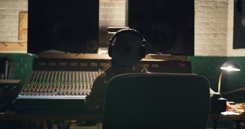 Sound engineer grooving to music she is working on at night in recording studio using a professional mixing board. Medium shot on 4K RED camera.