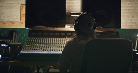 Young Asian woman sound producer dances to music she is working on at night in audio studio over professional mixing boards. Medium shot on 4K RED camera.