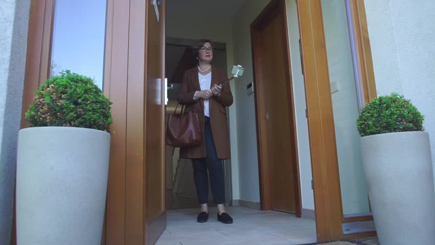 Mature woman in brown clothes stands in the doorway with smartphone selfie stick and shooting blogger podcast about career opportunities of internal auditor project manager.
Vlogger concept. Royalty-Free Stock Footage #1019088607