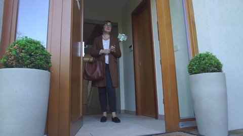Mature woman in brown clothes stands in the doorway with smartphone selfie stick and shooting blogger podcast about career opportunities of internal auditor project manager.
Vlogger concept.