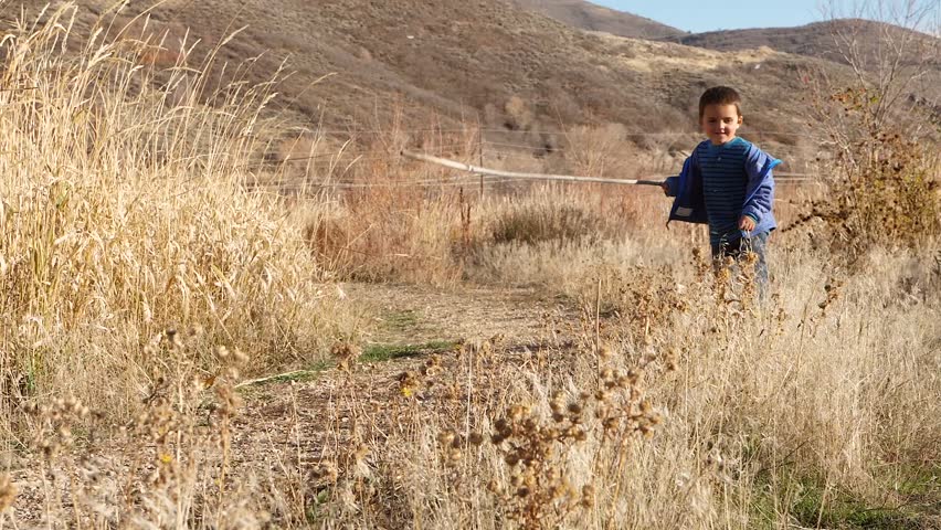 A slow motion shot of cute little brothers running through the tall golden grass on a trail at sunset
