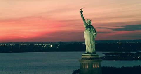 Aerial view of Statue of Liberty in New York under beautiful pink red summer sunset. Wide to Long shot on 4K RED camera.
