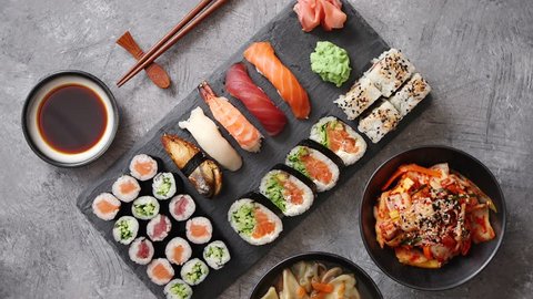 Japanese food composition. Various kinds of sushi placed on black stone board. Spicy kimchi salad, wontong soup, chopsticks and soy souce bowl.