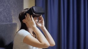Beautiful young woman wearing VR Headset at bedroom and looking around. Close-up watch VR video. Virtual reality concept. Close-up