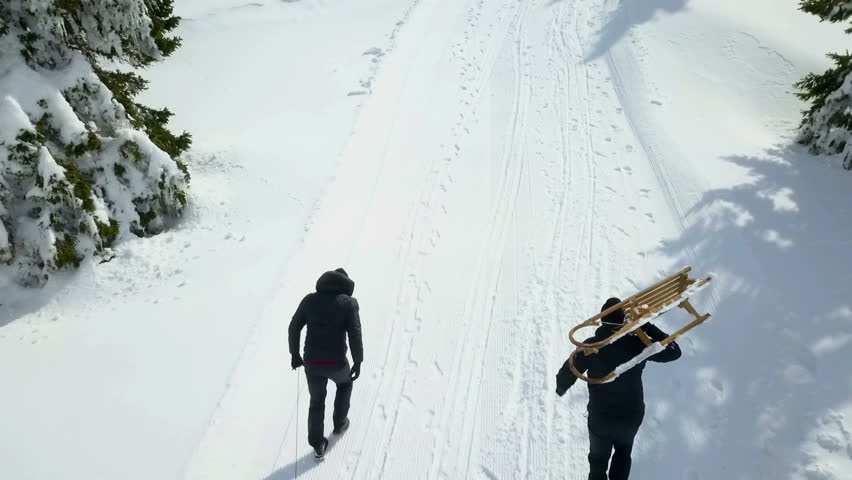 Two guys are pulling and carrying their sleighs uphill. It