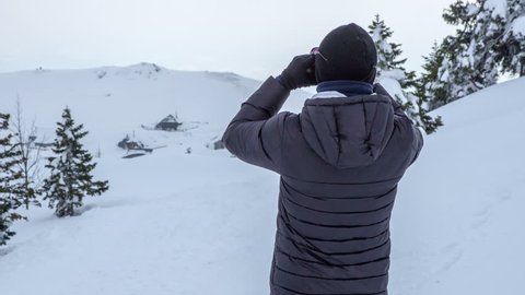 A man looks through binoculars and he is watching the snowy landscape.