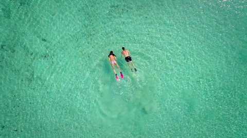 Aerial view of man and woman swimming and snorkeling with masks and flippers in clear sea.