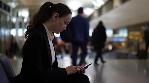 Woman look through images on smartphone, sit at airport hall, blurred background. Passenger lady spend time waiting for boarding at international terminal