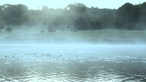 Blue mist of cold morning drifts over lake river