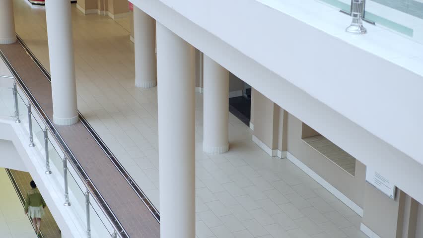 Two active young female friends walking in shopping mall and chatting, one of them holding handbag while another one carrying shopping bags, high angle view