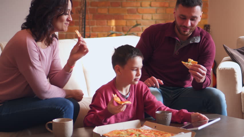 Family using digital tablet while eating pizza in living room