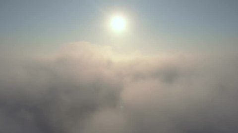 Aerial view over the clouds and sun is shining. Drone flying forward and through while clouds moving. Sun centered above