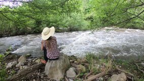 Young woman with a hat sitting by a river. Occitanie in the south of the France