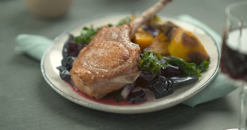 Pink sauce poured on rack of lamb in faience plate with salad and yellow turnip, on a blue towel, with a glass of red wine in the foreground. Close shot in slow motion in 4K on a Phantom Flex camera.