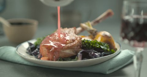 Pink sauce poured on rack of lamb in faience plate with salad and yellow turnip, on a blue towel. Slow motion 4K Phantom Flex.