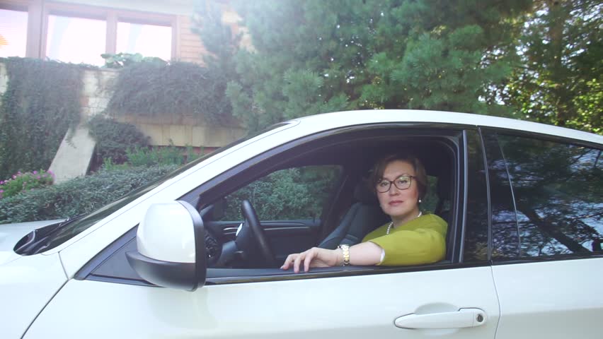 Stylish business woman looking out of the car window, prepares for blog subscribers monthly sales reports, dealership deals, reviews of current vehicles and future electric cars. 
Test drive review.