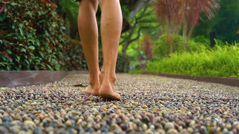 slowmotion shot of a young man walking on a reflexological path in a tropical park