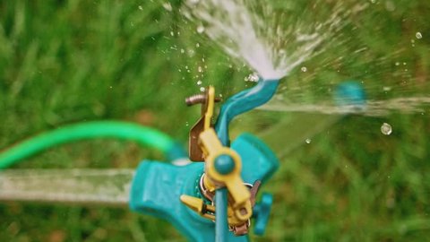 Top view of working head of garden sprinkler in slow-motion, pan right.
