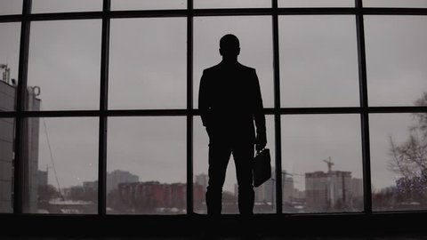 businessman stands at the window in the office and looks at the city. 4K