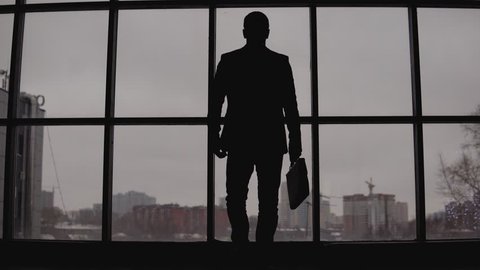 businessman with a case in hand goes to the window in the office and looks at the city