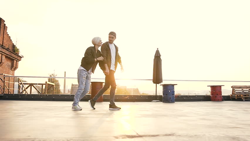 Handsome guy holds girlfriend by the hand and runs to multi-colored armchairs on terrace of the styl cafe. Outdoors. Happy couple having fun outdoors holding hands, running on the roof of terrace of