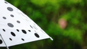 Close up of white and black umbrella raising against raindrops with natural blurred background
