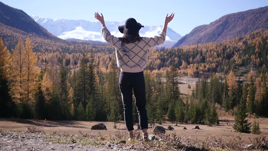 A woman with raised hands on top of a mountain looking at the view. The girl raises her hand up, noting the scenic landscape, enjoying nature, traveling adventure. Gorny Altai on the way to Mangolia