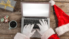 Digital composite of Video composition with snow over desk  with santa hand on laptop