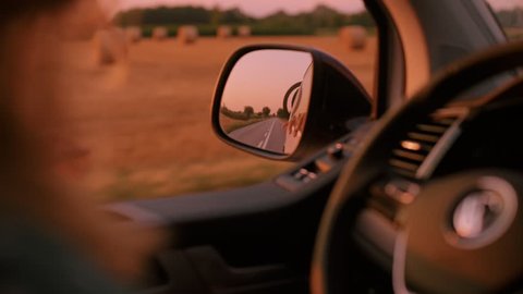 Reflection in car side mirror of camping van with bike rack. Young woman embarks on summer holiday adventure, moves hand in wind, drives caravan with one hand on steering wheel. Vanlife lifestyle
