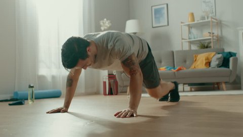 Strong Muscular Athletic Fit Man in T-shirt and Shorts is Doing Mountain Climber Exercises at Home in His Spacious and Bright Living Room with Minimalistic Interior.