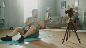 Strong Athletic Fit Man in T-shirt and Shorts is Recording his Crisscross Crunch Workout on Camera for His Blog. Scene takes place in His Spacious and Bright Living Room with Minimalistic Interior.