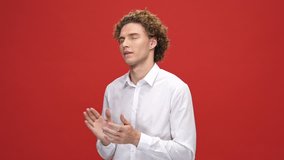 Pleased curly man in business shirt having fun and dancing over red background
