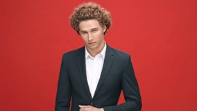 Cool confident curly man in business suit pointing and looking at the camera over red background